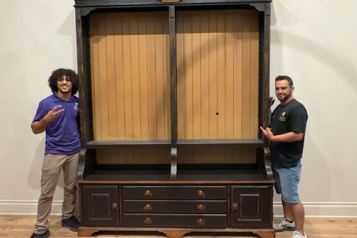 Two Trinity Movers crew members standing beside a tall antique armoire placed on a patterned rug