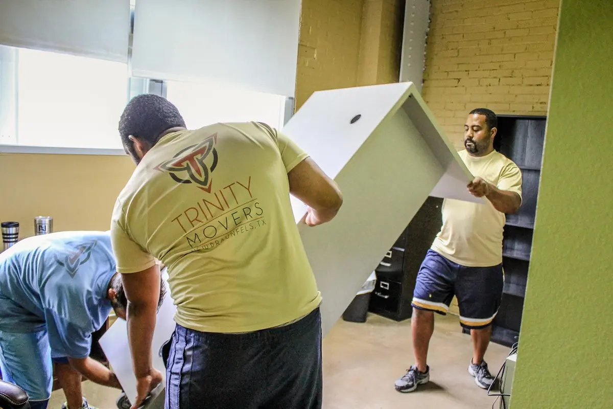 Three Trinity Movers crew members in company shirts tilting a white cabinet as they carry it