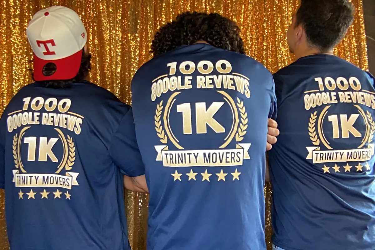 Three Trinity Movers crew members seen from behind in matching shirts celebrating 1,000 Google reviews