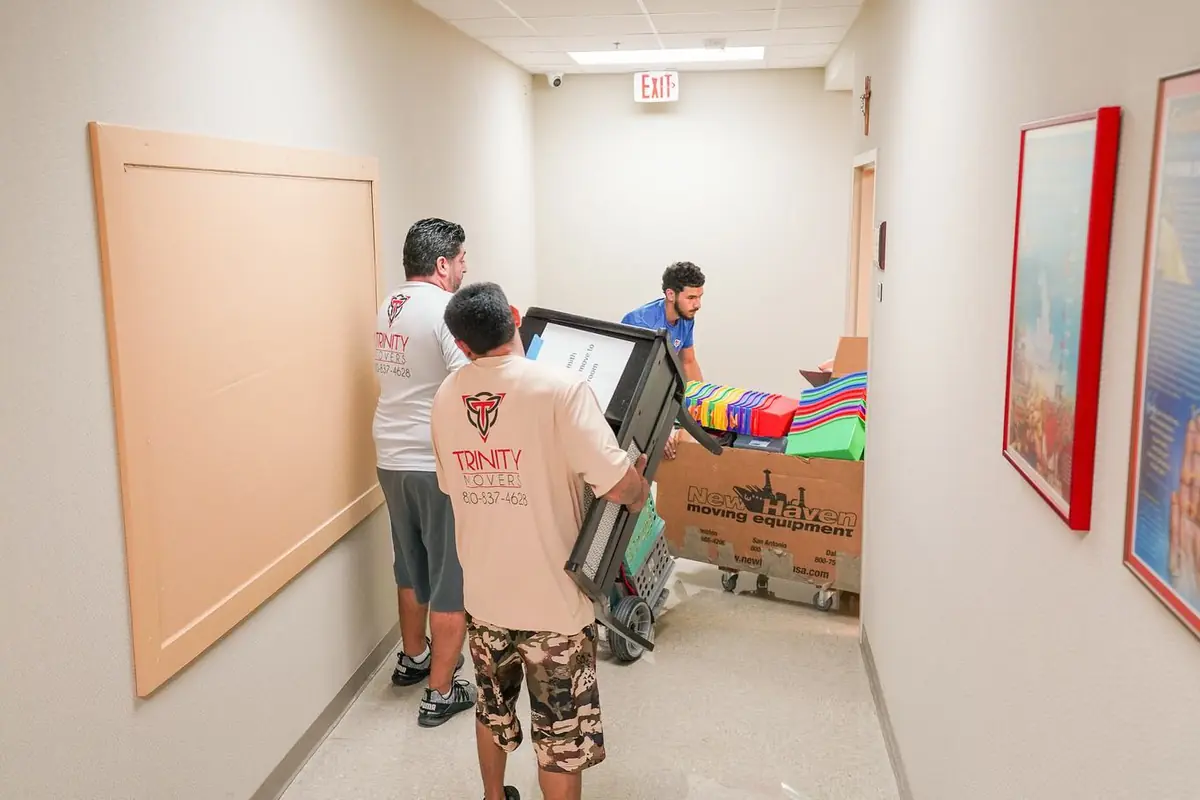 Trinity Movers crew members wheeling a loaded cart down an interior hallway beneath an exit sign