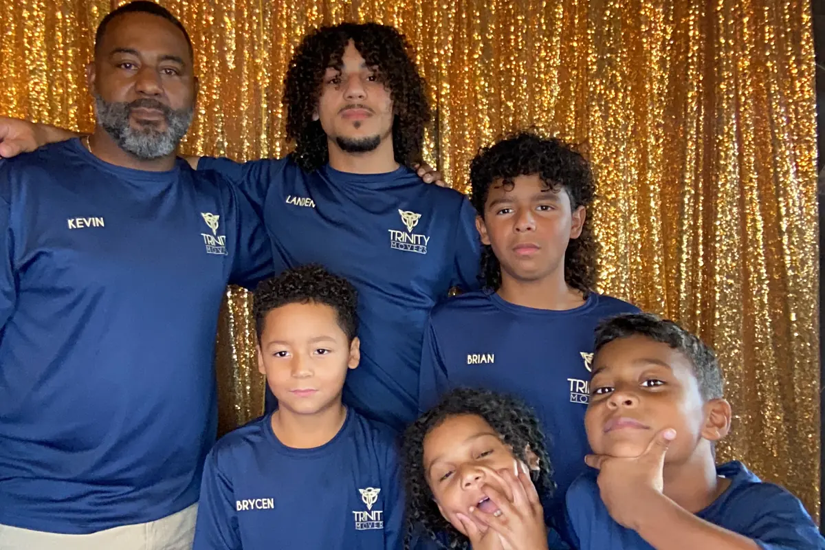 Kevin Joshua and his children in matching Trinity Movers shirts in front of a gold backdrop