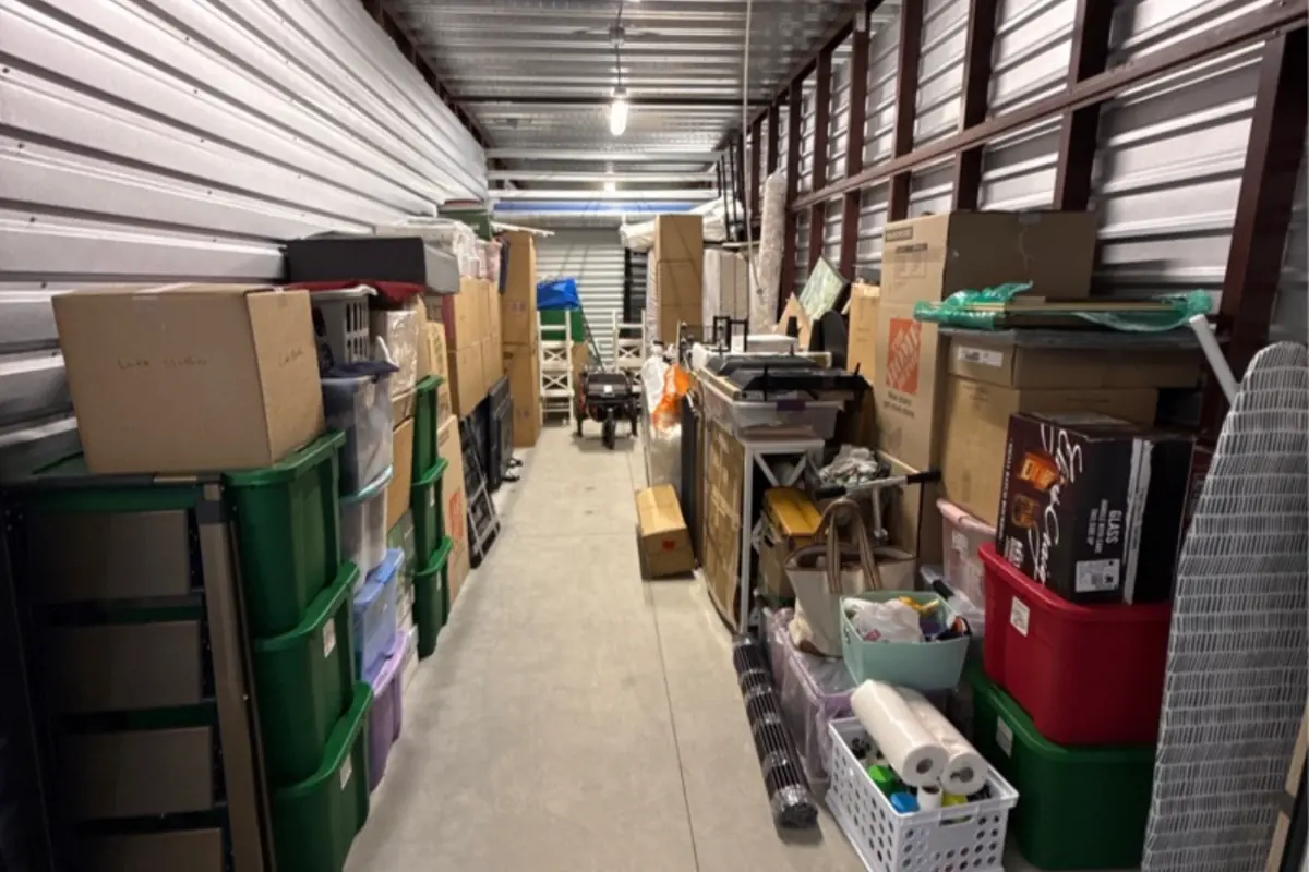 Long aisle inside a storage facility lined with stacked bins, boxes, and wrapped furniture