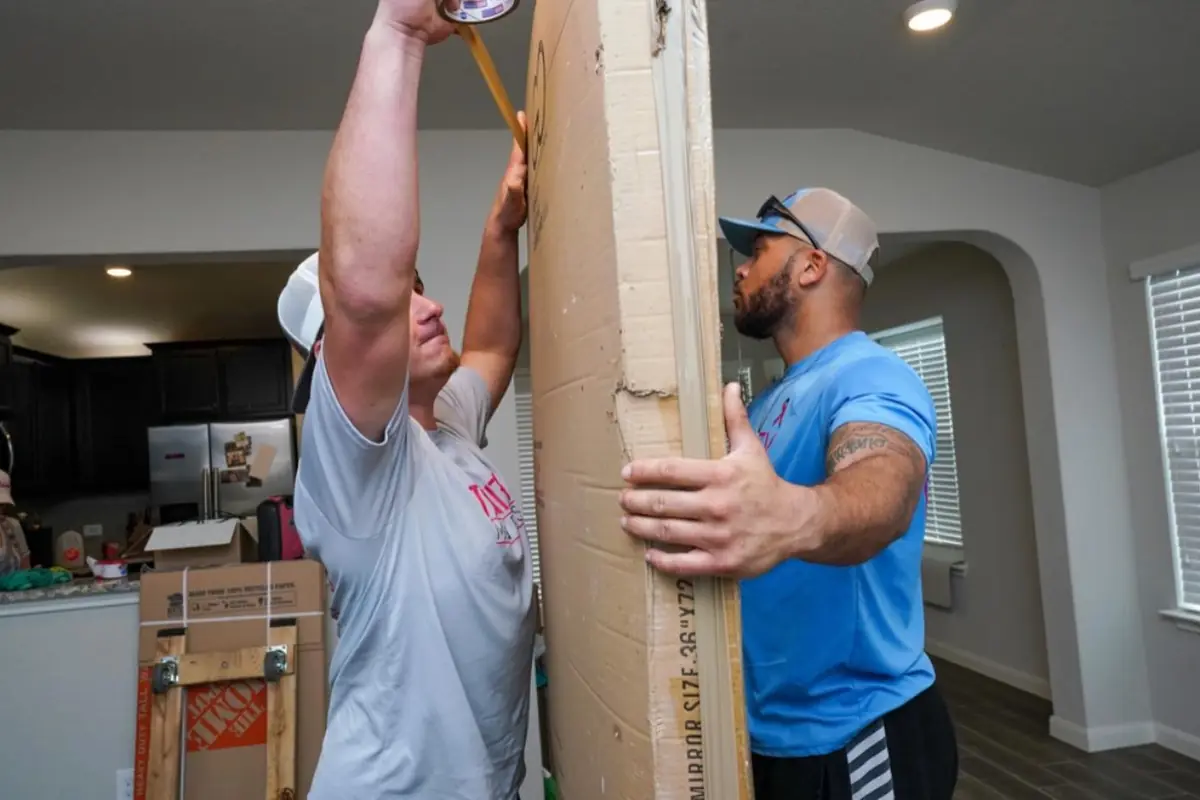 Two Trinity Movers crew members taping up a tall mirror carton inside a home