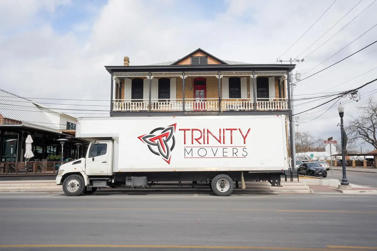 White Trinity Movers box truck parked on a street in front of a two-story historic building