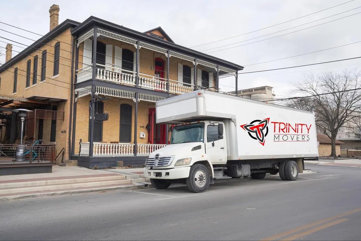 Trinity Movers box truck parked along a street beside a two-story brick building with wraparound balconies