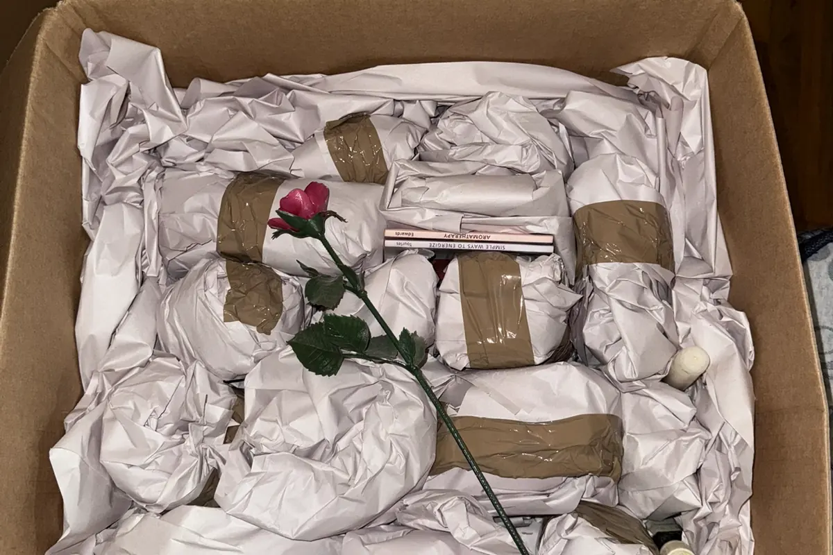 Open moving box packed with paper-wrapped items, with a single rose laid on top